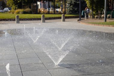 Su damlacıkları havadaki çeşmeden yayıldı. Parktaki fıskiyeden su sıçratmak. Şehir parkındaki meydanda kaldırımda dikey fıskiye fıskiyeleri