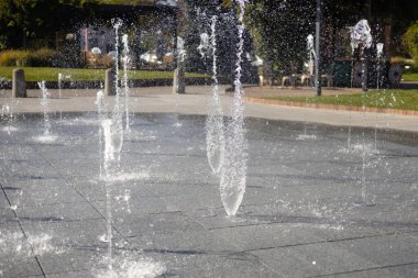 Su damlacıkları havadaki çeşmeden yayıldı. Parktaki fıskiyeden su sıçratmak. Şehir parkındaki meydanda kaldırımda dikey fıskiye fıskiyeleri