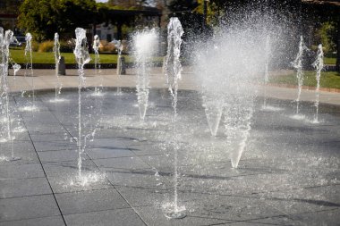 Su damlacıkları havadaki çeşmeden yayıldı. Parktaki fıskiyeden su sıçratmak. Şehir parkındaki meydanda kaldırımda dikey fıskiye fıskiyeleri