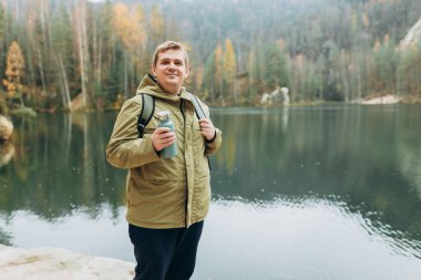 Sırt çantalı gülümseyen bir erkek gezgin görkemli gölün güzel manzarasının tadını çıkarıyor. Seyahat, macera. Etkin bir yaşam biçimi kavramı.