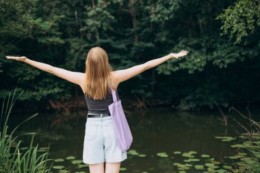Doğada tuvalden yapılmış bir alışveriş çantası olan genç bir kadın. 30 'lu yaşlardaki kadın su zambaklarıyla botanik bahçesinde poz veriyor. Model