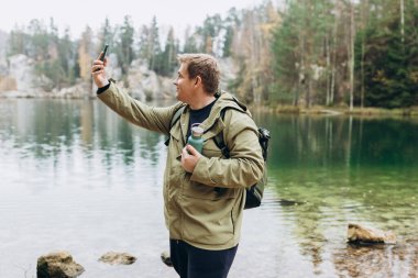Mutlu yakışıklı adam dışarıda tatilde bir selfie portresi çekiyor. Görkemli gölün yanında duran bir gezgin. Seyahat, macera. Etkin bir yaşam biçimi kavramı.