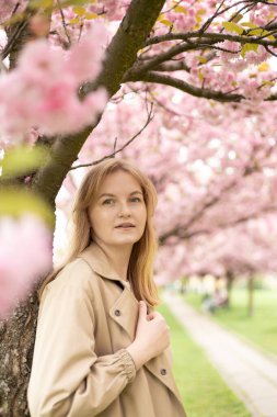 Genç, güzel, gülümseyen, 30 'lu yaşlarda, moda elbiseli, botanik bahçesinde duran bir hippi. Çiçek açan ağaçlarda poz veren kaygısız kadın. Çiçek açan bahçede bir kız. Kadınlar için bayrak