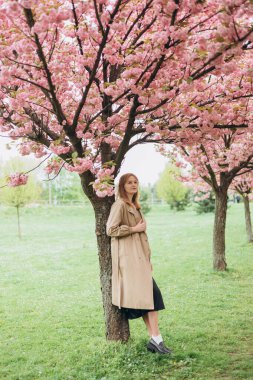 Genç, güzel, gülümseyen, 30 'lu yaşlarda, moda elbiseli, botanik bahçesinde duran bir hippi. Çiçek açan ağaçlarda poz veren kaygısız kadın. Çiçek açan bahçede bir kız. Kadınlar için bayrak