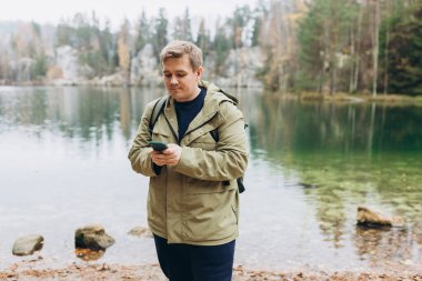 Sırt çantalı gezgin telefonu görkemli gölün yanında duruyor. Seyahat, macera. Aktif yaşam tarzı kavramı. Yüksek kalite fotoğraf.