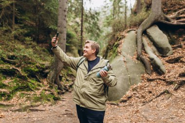 Ormanda yürüyüş yapan ve vahşi hayatın fotoğrafını çeken 30 'lu yılların kutlu olsun. Genç erkek dışarıda selfie çekiyor. Yürüyüş, yaşam tarzı, macera ve turizm konsepti