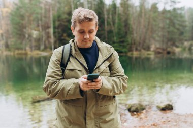 Sırt çantalı gezgin telefonu görkemli gölün yanında duruyor. Seyahat, macera. Aktif yaşam tarzı kavramı. Yüksek kalite fotoğraf.