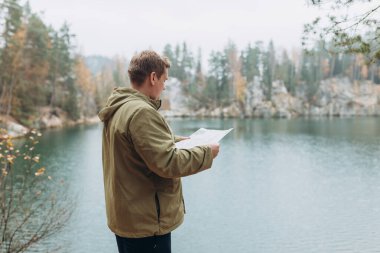 Sırt çantalı gezgin elinde kağıt haritayla görkemli göl kıyısında duruyor. Seyahat, macera. Aktif yaşam tarzı kavramı. Yüksek kalite fotoğraf