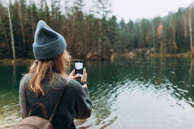 Şapkalı kişi, vahşi doğa arka planında göl kenarında akıllı bir telefonla içeriği kaydediyor. Dışarıda telefonla dolaşan 30 'lu yaşlarda şık bir kız. Seyahat, macera. Etkin bir yaşam biçimi kavramı