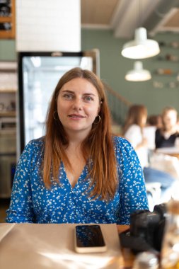 30 'lu yaşlardaki mutlu kızıl saçlı kadın kafede bekliyor.