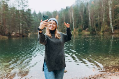 Mutlu sarışın kadın, dağ gölü manzarasının tadını çıkarırken selfie çekiyor. Doğa özgürlüğü macerası, tatil videosu, kız turist açık hava.