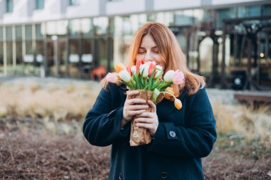 İlkbahar laleli güzel bir kadın çiçek buketi ile şehir caddesinde yürüyor. Dışarıda poz veren mutlu kız. Kentsel arka planda güzel bir kadının bahar portresi