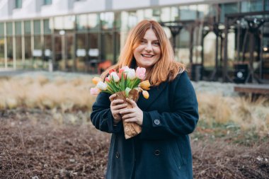 İlkbahar laleli güzel bir kadın çiçek buketi ile şehir caddesinde yürüyor. Dışarıda poz veren mutlu kız. Kentsel arka planda güzel bir kadının bahar portresi