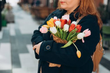 İlkbahar laleli güzel bir kadın çiçek buketi ile şehir caddesinde yürüyor. Dışarıda poz veren mutlu kız. Kentsel arka planda güzel bir kadının bahar portresi