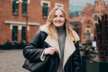 Şehir caddesinde kışın giydiği kıyafetle gezen 30 'lu yaşlardaki çekici, genç bir kadın. Şehir yaşam tarzı konsepti. Dışarıdaki kameraya bakan mutlu kadın portresi. Yüksek kalite fotoğraf