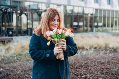 İlkbahar laleli güzel bir kadın çiçek buketi ile şehir caddesinde yürüyor. Dışarıda poz veren mutlu kız. Kentsel arka planda güzel bir kadının bahar portresi