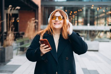 Kablosuz kulaklıklı, telefon dinleyen, müzik dinleyen, açık havada, üniversite kampüsünde ses dersinin tadını çıkaran 30 'lu yılların beyaz bayan öğrencisi. Şehir geçmişinde akıllı telefonu elinde tutan Mutlu Kadın.