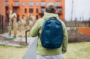 Sırt çantalı bir adam şehirde sokakta yürüyor. Şehir yaşam tarzı konsepti. Gezgin. Bahar geldi. Dışarıda dikilen günlük elbiseli genç adam..