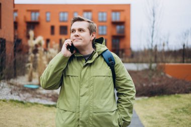 Genç sarışın adam gülümsüyor. Kendine güveniyor. Akıllı telefondan konuşuyor..