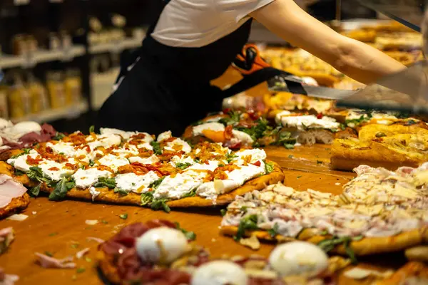 Sicilya usulü dikdörtgen peynirli ve domatesli pizzadan bir dilim servis ediyorum. İtalya 'da bir restoranın vitrininde otantik İtalyan pizzası.
