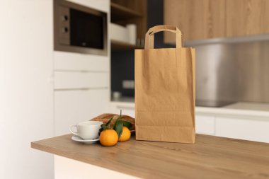 Bir fincan kahve, turunçgil ve sandviçle ahşap mutfak tezgahında alışveriş torbası.