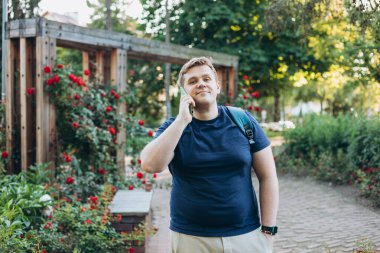 Şehir parkında 30 'lu yaşlardaki mutlu sarışın adam akıllı telefondan konuşuyor.