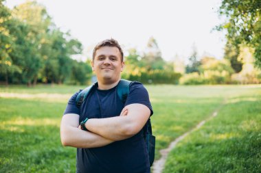 Kırsalda duran sırt çantalı 30 'lu yaşlarda sarışın bir adam. Gezgin. Yaz zamanı. Açık havada dikilen sıradan giysili mutlu genç adamın portresi.