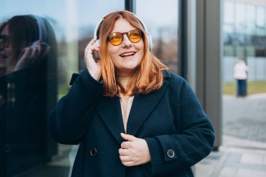 Kablosuz kulaklık takan 30 'lu yılların beyaz bayan öğrencisi müzik dinliyor, üniversite kampüsünde ve açık havada müzik dersinin tadını çıkarıyor. Şehir geçmişinde duran Mutlu Kadın