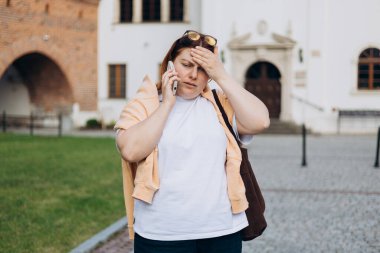 Sokakta cep telefonuyla konuşan stresli genç bir kadın.