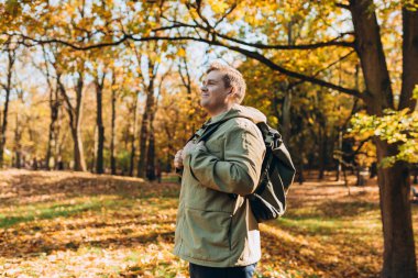 Autumn Park 'ta rahatlayan mutlu 30' lu yaşlarda bir adam. Gezgin. Düşme zamanı. Dışarıda dikilen, günlük kıyafetli, gülümseyen adam.