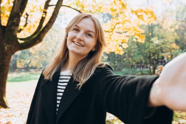 Sonbahar parkında selfie çeken siyah ceketli mutlu kadın portresi. Seyahat, yaşam tarzı, insanlar ve hobi kavramı.