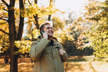 30 'lu yaşlarda akıllı telefondan konuşan mutlu bir adam. Teknoloji cep telefonu. Beyaz bir erkek, gülümsüyor. Parktaki akıllı telefondan konuşuyor..