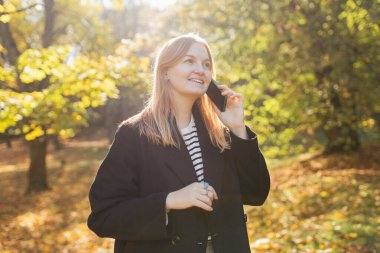 Şehrin sonbahar parkında telefonla konuşan 30 'lu yaşlardaki güzel bir kadının portresi. Sonbahar geldi. Dışarıda dikilen günlük elbiseli genç bir kadın.
