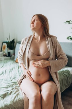 Sırt ağrısı çeken mutsuz bir kadın yatakta oturuyor. Geçen ay hamile kalan yorgun, sarışın bir kadın, hamileliğinden dolayı acı çekiyor. Kadın karnına sarılıp bebeğine dokunuyor.