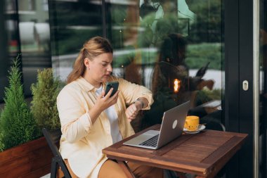Kafkasyalı serbest çalışan kadın açık kafedeki boş laptopta uzaktan kumanda için takılabilir kol saatini kontrol ediyor.