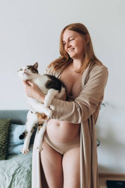 Hamile kadınlar kediye yataklık eder. Genç, hamile, sarışın bir kadın ve büyük kedisi. Evcil hayvan sahibi evde.