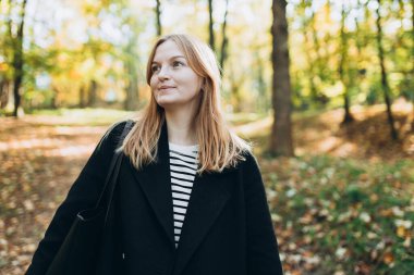 Sonbahar parkında sarı yaprakları dökülmüş genç bir kadın. Sonbahar mevsimi konsepti