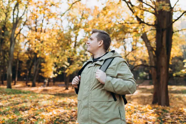 Autumn Park 'ta rahatlayan mutlu 30' lu yaşlarda bir adam. Gezgin. Düşme zamanı. Dışarıda dikilen, günlük kıyafetli, gülümseyen adam.
