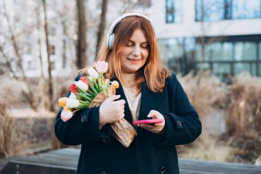 Kablosuz kulaklıklı, telefon dinleyen, müzik dinleyen, açık havada, üniversite kampüsünde ses dersinin tadını çıkaran 30 'lu yılların beyaz bayan öğrencisi. Şehir geçmişinde akıllı telefonu elinde tutan Mutlu Kadın.