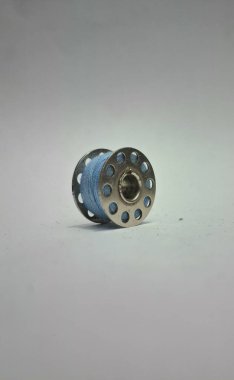 Beyaz zemin üzerinde izole edilmiş mavi iplik içeren bir metal dikiş makinesi bobbin.