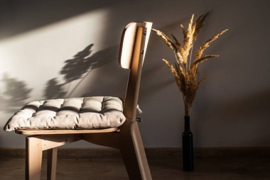 Kurumuş çiçeklerle dolu, batan güneşin ışınlarında yastıklı, basit, açık ahşap bir sandalye.