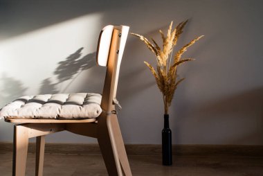 Kurumuş çiçeklerle dolu, batan güneşin ışınlarında yastıklı, basit, açık ahşap bir sandalye.