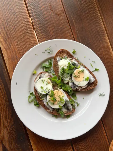 stock image Sprat Sandwich served on a plate- traditional Latvian cuisine appetizer with salted sprat, butter, boiled egg, fresh onion and herbs on a slice of rye bread