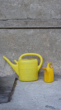 Verandada duran iki plastik sarı sulama kutusu. Bahçedeki su bidonları bahçede kullanılmayı bekliyor.. 