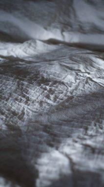 Yatak odasında sabah güneşiyle desenli beyaz çarşaflar. Yatak üstüne uyku konsepti. Buruşuk çarşaf ve yorgan tekstili. Kumaş ve keten arkaplan.