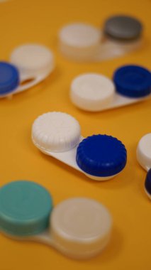 Farklı kontak lens kapları ya da kutular. Temizlik çözeltisi. Sarı arka plan. Düz yatıyordu