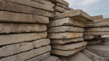 Düz beton levhalar üst üste yığılmış. Yıpranmış ve pürüzlü kenarları var. Açık gökyüzünün altında açık hava manzarası. İnşaat malzemeleri ve endüstriyel gelişim görüntüleri