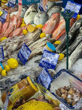 Balık, kabuklu deniz ürünleri ve baharatlar da dahil olmak üzere çeşitli taze deniz ürünleri sergileniyor, limon süslemeleriyle servis ediliyor, bir pazar yerinde buza konuyor, tazelik ve mutfak çeşitliliği sergiliyor..