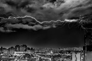 A dramatic black and white photo of a lightning storm over a cityscape at night. Bolts illuminate dark clouds and buildings, creating an intense atmosphere. City lights contrast with the ominous sky, showcasing nature's power. clipart