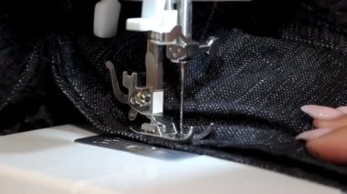 Video, gri kumaşı diken dikiş makinesi iğnesinin yakın çekimini gösteriyor. Dikiş sürecinin ustalığını ve inceliğini vurguluyor, düzgün ve hatta dikişler yaratıyor..
